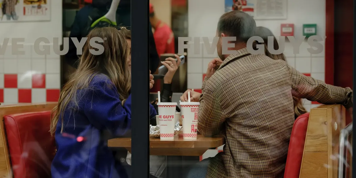 A group of friends share a meal and conversation at Five Guys, visible through the window.