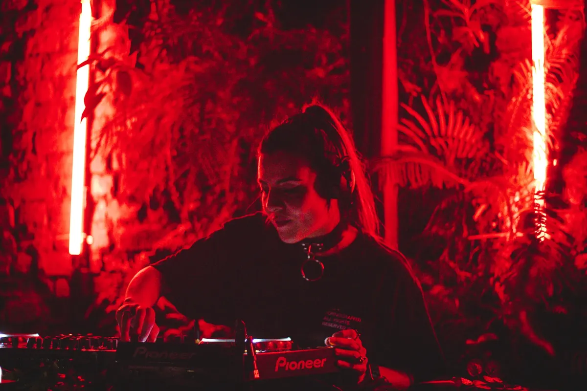 A female DJ immersed in her music, creating an electrifying atmosphere in a nightclub with vibrant lighting.