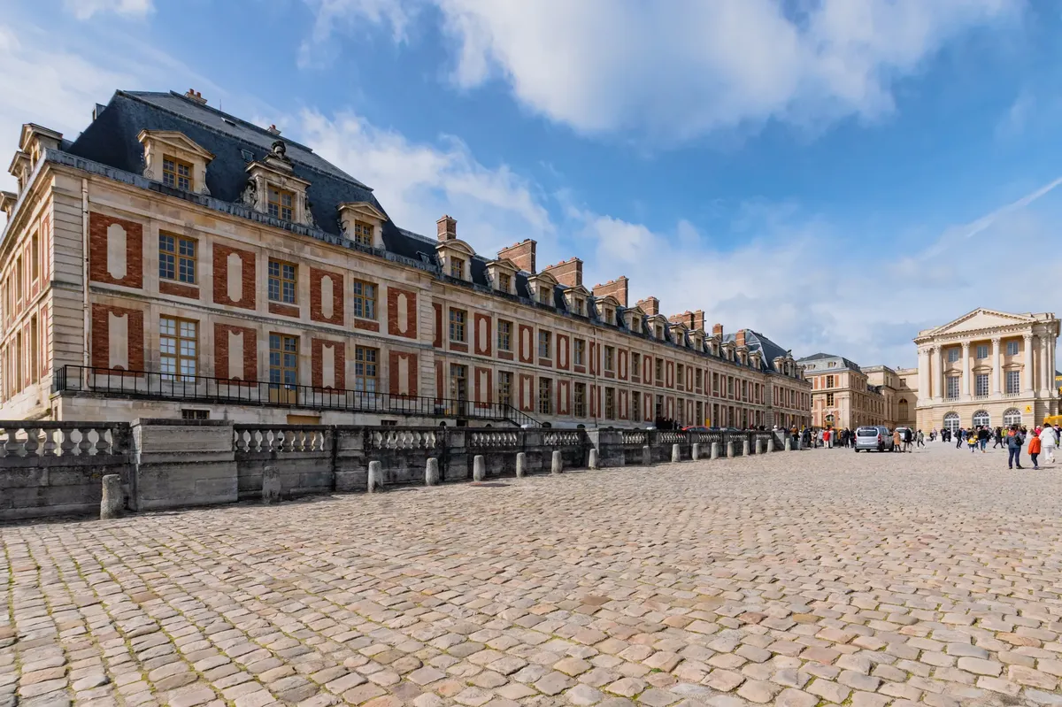 Stunning view of the Palace of Versailles exterior, showcasing baroque architecture under a blue sky.