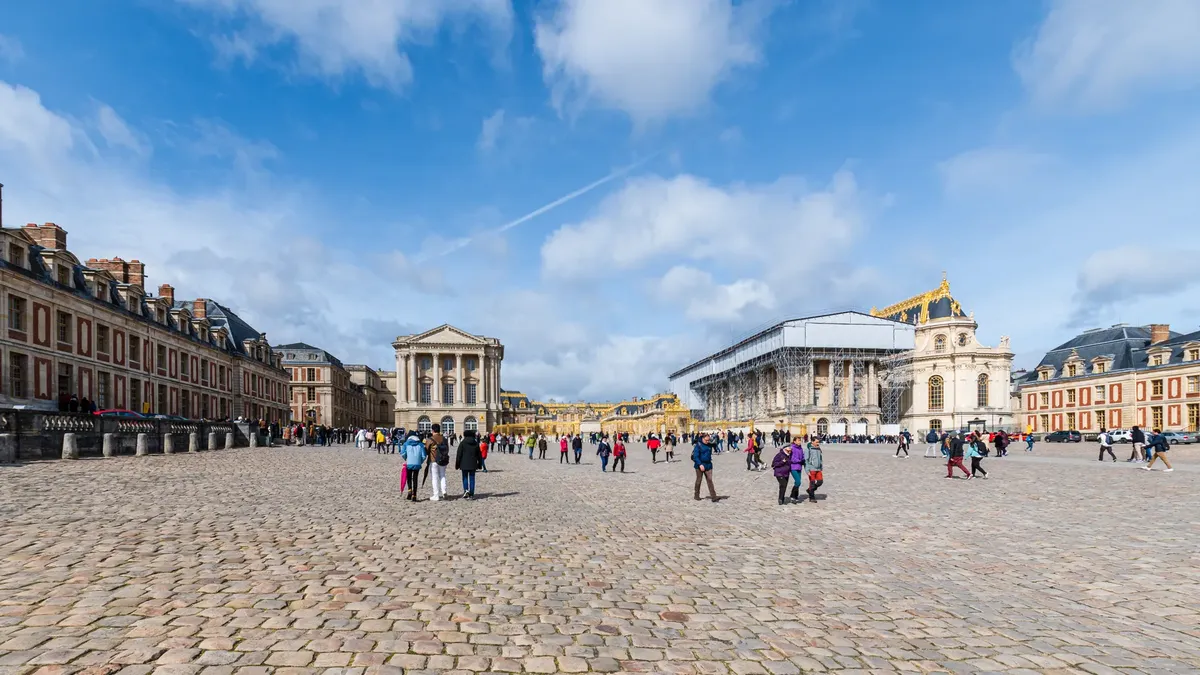 A vibrant scene of tourists exploring the historic Palace of Versailles in Paris, France.