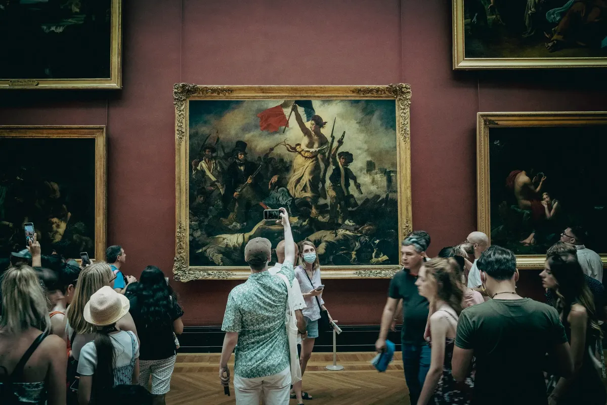 Crowd admires and photographs iconic art in the Louvre Museum, Paris.