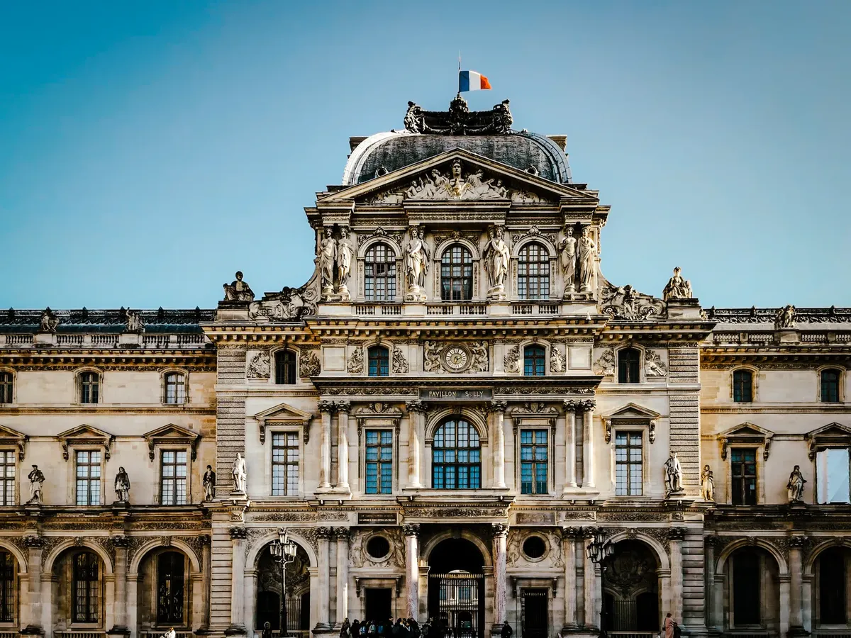 Classic baroque architecture of the iconic Louvre Museum in Paris, adorned with the French flag under a clear sky.